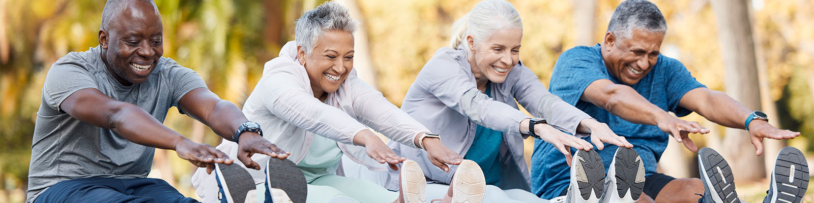 Four male and female senior living residents sitting down stretching while wearing exercise clothes