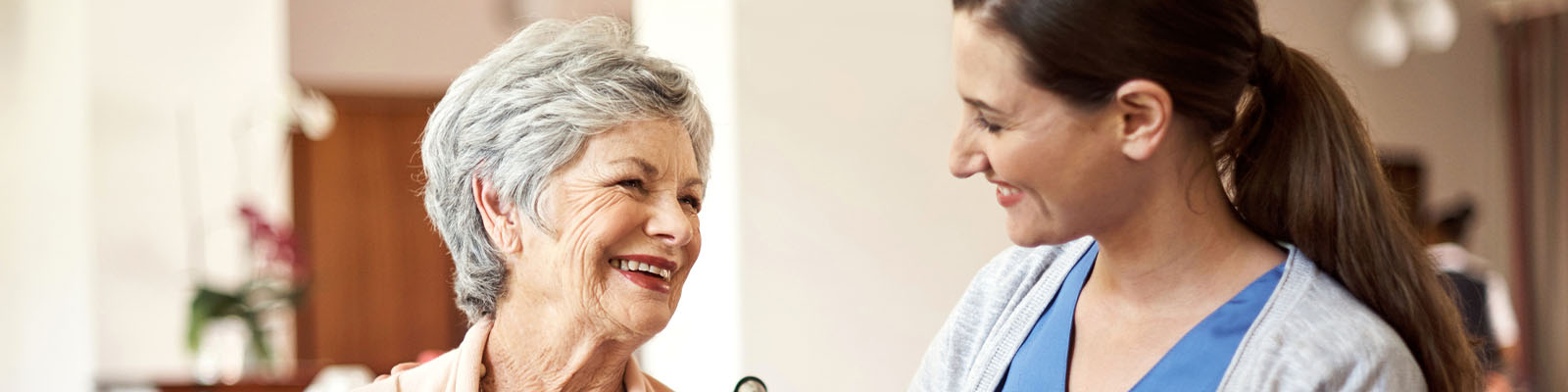 A female senior living resident smiling and looking at her female nursing assistant