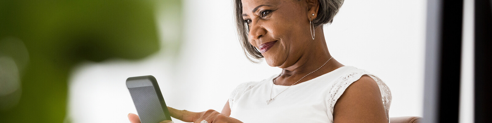 A senior woman wearing a white shirt smiling while looking down and scrolling on her phone