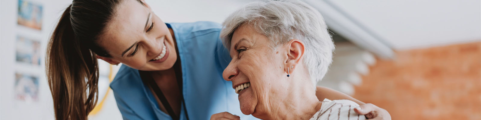 A female senior living resident looking up at her female nursing assistant while smilinh